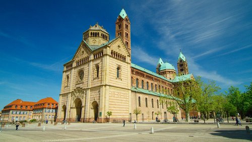Der Dom zu Speyer in Speyer am Rhein unter blauem Himmel mit einem gepflasterten Platz im Vordergrund auf dem Menschen spazieren.