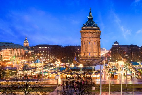 Weihnachtsmarkt in Mannheim bei Nacht, mit festlich beleuchteten Ständen und einem großen Turm im Zentrum.