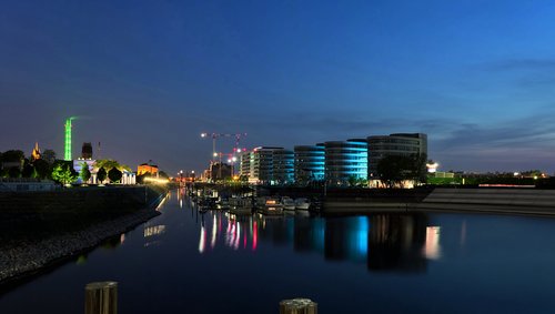 Blick auf den Duisburger Hafen bei Nacht.Boote und beleuchtete Gebäude am Rheinufer unter klarem Himmel.