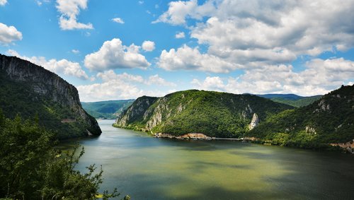 Blick auf die Katarakten der Donau mit ruhigem, grünblauen Wasser, umgeben von tiefgrüner Vegetation und felsigen Ufern.