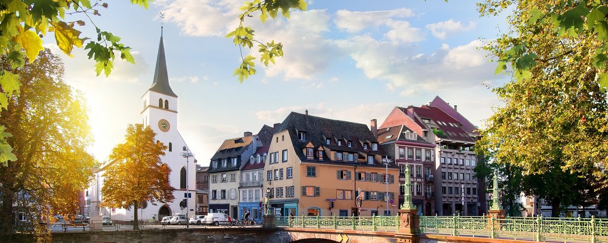 Straßburger Altstadt mit Fachwerkhäusern und der Kathedrale im Hintergrund, umgeben von Bäumen und einem Fluss bei Sonnenuntergang.