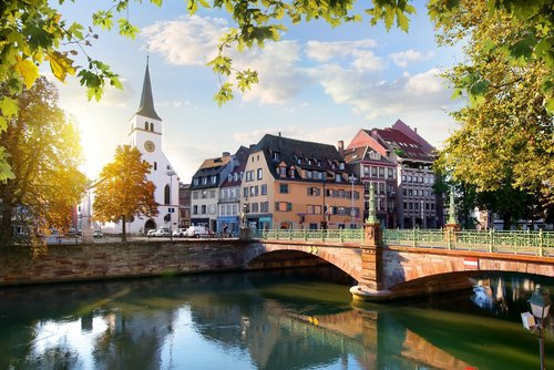 Straßburger Altstadt mit Fachwerkhäusern und der Kathedrale im Hintergrund, umgeben von Bäumen und einem Fluss bei Sonnenuntergang.