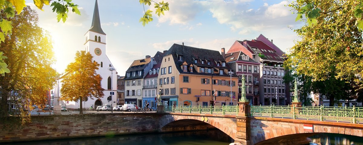 Straßburger Altstadt mit Fachwerkhäusern und der Kathedrale im Hintergrund, umgeben von Bäumen und einem Fluss bei Sonnenuntergang.