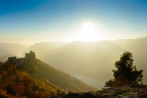 Sonnenaufgang über der herbstlichen Landschaft der Wachau mit Burgruine auf einem Hügel und Nebel im Tal