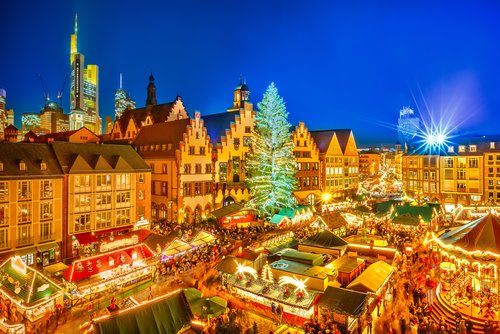 Weihnachtsmarkt in der Altstadt von Frankfurt am Main bei Nacht, mit festlich beleuchteten Ständen und einem großen, geschmückten Weihnachtsbaum und Hochhäusern im Hintergrund.