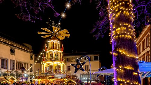 Weihnachtlich geschmückter Marktplatz in Aschaffenburg bei Nacht, mit beleuchteten Ständen und einer großen Weihnachtspyramide im Zentrum.