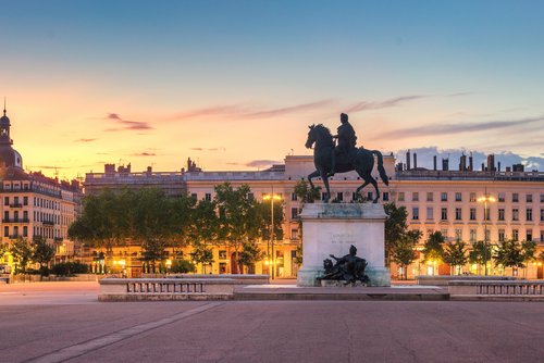 Reiterstatue auf einem Platz in Lyon bei Sonnenuntergang, umgeben von historischen Gebäuden und Bäumen