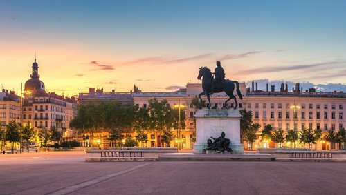 Reiterstatue auf einem Platz in Lyon bei Sonnenuntergang, umgeben von historischen Gebäuden und Bäumen