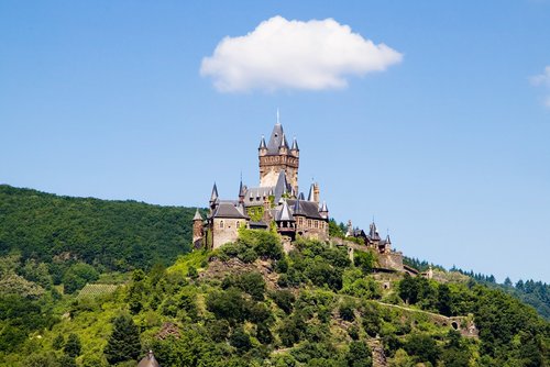Reichsburg Cochem thront auf einem Hügel, umgeben von bewachsenen Hügeln an der Mosel, mit Blick auf die Stadt Cochem und den Fluss.