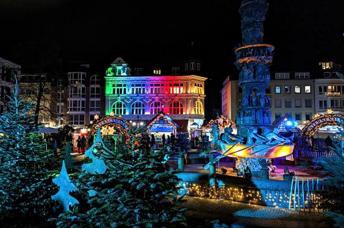 Weihnachtsmarkt in Koblenz bei Nacht mit bunt beleuchtetem historischen Gebäude, geschmückten Tannenbäumen und einem beleuchteten Brunnen mit Figuren