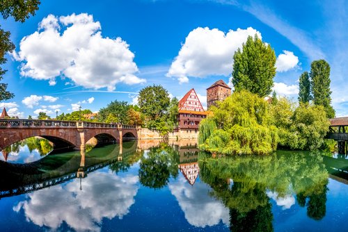 Fluss in Nürnberg mit Brücken, die diesen rechts und links überspannen und historischen Gebäuden im Hintegrrund bei blauem Himmel