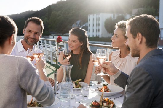 Yvonne Catterfeld und vier weitere Personen sitzen beim Abendessen und Wein auf dem Sonnendeck, Sonnenlicht im Hintergrund.