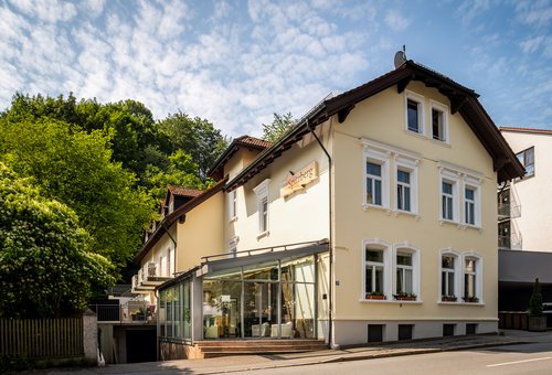 Außenansicht des Hotel Spitzberg in Passau mit einem Wintergarten, umgeben von grünen Bäumen an einer Straße liegend.