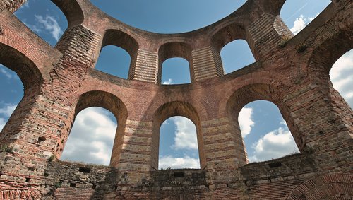 Ruinen der Kaiserthermen in Trier, mit altertümlichen Steinmauern und Bögen, mit blauem Himmel im Hintergrund.
