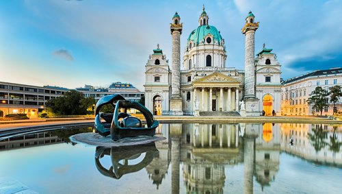 Barocke Karlskirche mit zwei Säulen und grünem Kuppeldach in Wien, Spiegelung im Wasserbecken mit moderner Skulptur