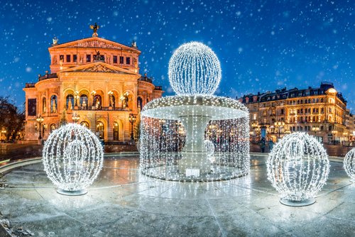 Die Alte Oper in Frankfurt bei Nacht und mit einem weihnachtlich beleuchteten Brunnen im Vordergrund. Es rieselt Schnee