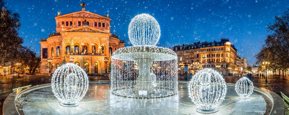 Die Alte Oper in Frankfurt bei Nacht und mit einem weihnachtlich beleuchteten Brunnen im Vordergrund. Es rieselt Schnee