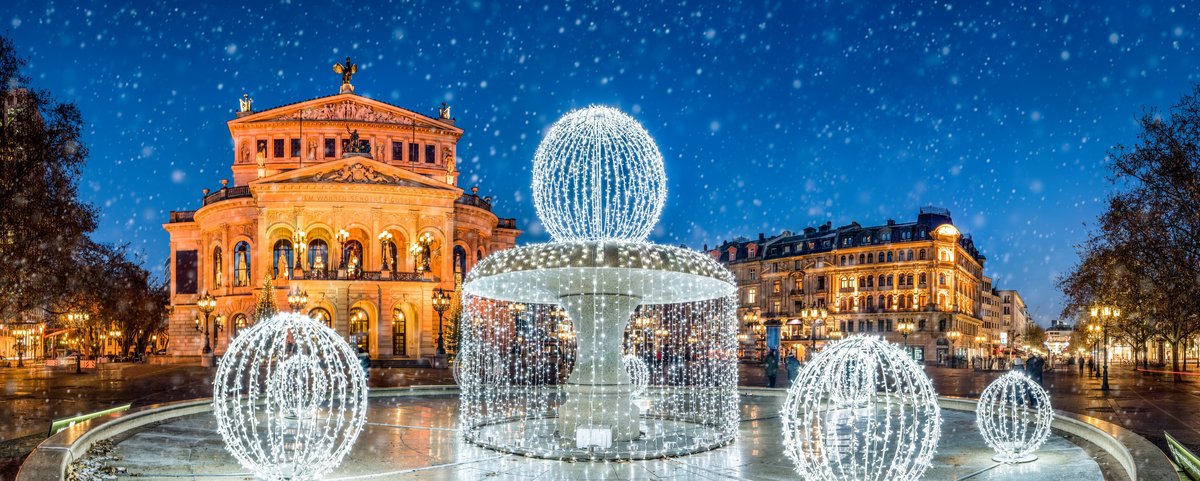 Die Alte Oper in Frankfurt bei Nacht und mit einem weihnachtlich beleuchteten Brunnen im Vordergrund. Es rieselt Schnee