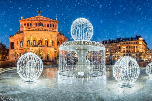 Die Alte Oper in Frankfurt bei Nacht und mit einem weihnachtlich beleuchteten Brunnen im Vordergrund. Es rieselt Schnee