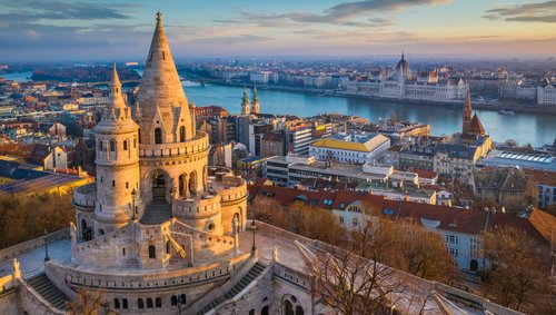 Blick auf die historische Fischerbastei in Budapest. Im Hintergrund ein Blick auf das Parlamentsgebäude von Budapest und über die Stadt bei Sonnenuntergang.