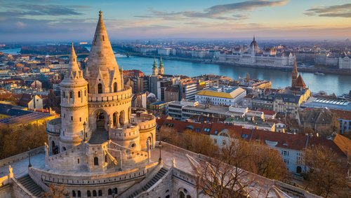 Blick auf die historische Fischerbastei in Budapest. Im Hintergrund ein Blick auf das Parlamentsgebäude von Budapest und über die Stadt bei Sonnenuntergang.