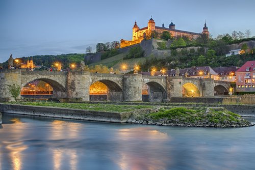 Festung Marienberg und Alte Mainbrücke in Würzburg bei Abenddämmerung mit beleuchteten Gebäuden und ruhigem Fluss