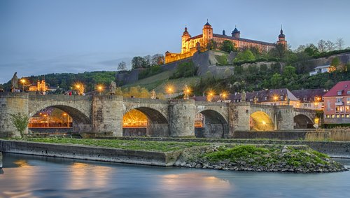 Festung Marienberg und Alte Mainbrücke in Würzburg bei Abenddämmerung mit beleuchteten Gebäuden und ruhigem Fluss