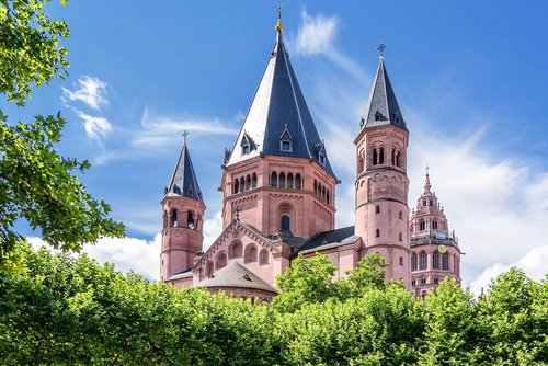Der Mainzer Dom mit seinen markanten roten Türmen und Spitzen, umgeben von grünen Bäumen unter blauem Himmel