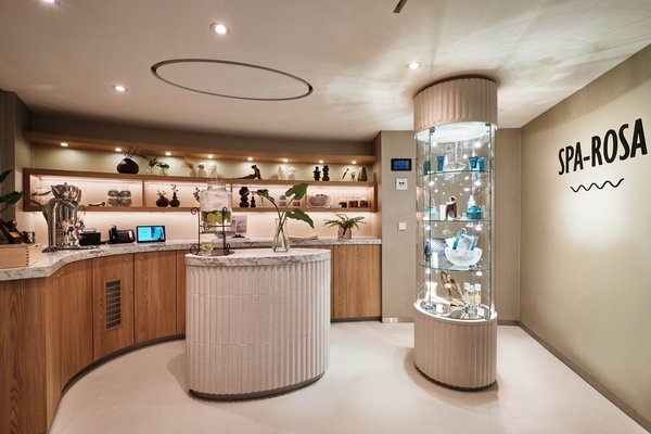 Empfangsbereich des SPA-ROSA mit dekorativen Regalen, Marmorinsel und Glasvitrine mit Produkten neben einem Treppenaufgang.