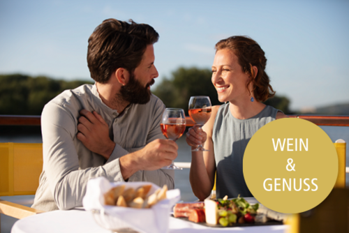 Ein Paar genießt Wein und Käseplatte auf dem Sonnendeck eines Flusskreuzfahrtschiffes, im Hintergrund grüne Bäume und blauer Himmel. Text "Wein & Genuss"