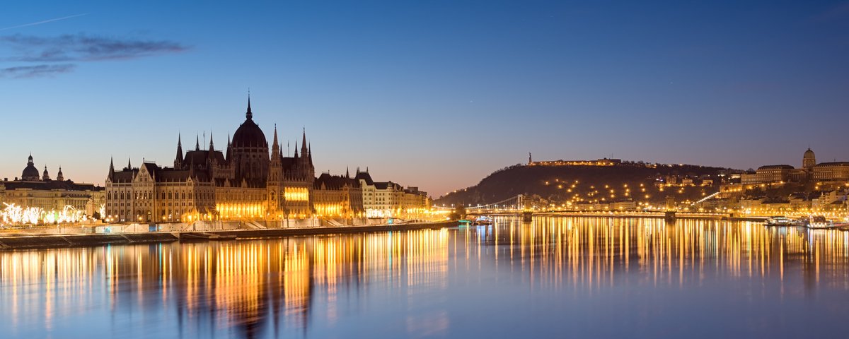 Blick auf das parlamentsgebäude in Budapest bei Nacht beleuchtet, mit der Stadt im Hintergrund.
