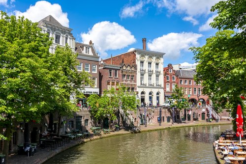 Historische Gebäude und Cafés entlang eines Kanals in Utrecht bei sonnigem Wetter mit blauem Himmel und grünen Bäumen