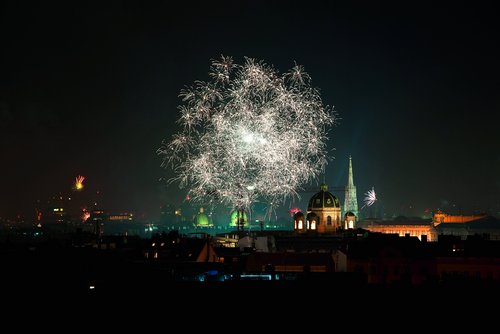 Feuerwerk über der nächtlichen Skyline von Wien mit beleuchteten historischen Gebäuden und dunklem Himmel.