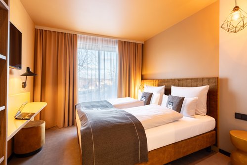 Hotelzimmer im Hotel Niu Flux Passau mit Doppelbett und Schreibtisch mit Hocker, modern eingerichtet in warmen Farben.