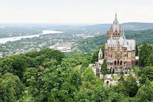 Blick auf das Schloss Drachenburg in Königswinter nahe Bonn, umgeben von üppiger Natur. Im Hintergrund Königswinter an der Donau.