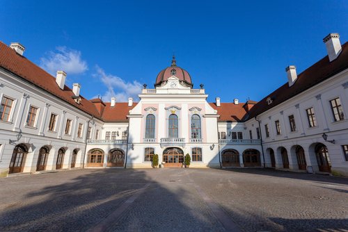 Der Eingang zu Schloss Gödöllő in Budapest unter blauem Himmel, davor ein gepflasterter Hof.