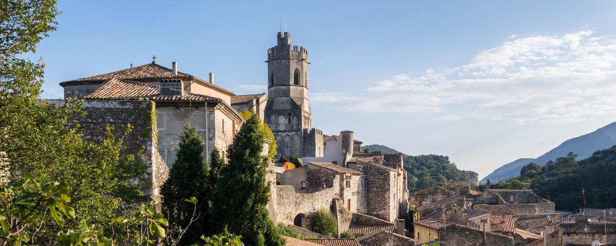 Mittelalterliche Burg in Viviers umgeben von grüner Vegetation und historischen Gebäuden bei blauem Himmel