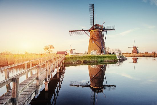Traditionelle niederländische Windmühlen in einer grünen Landschaft mit blauem Himmel am Kanal von Rotterdam. Im Vordergrund eine schmale Holzbrücke über dem Kanal.