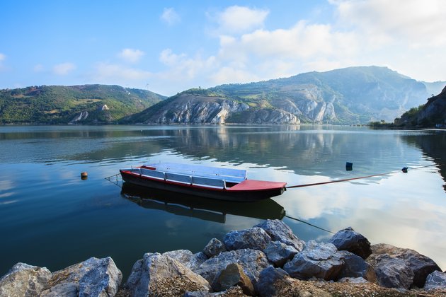 Rotes Fischerboot auf ruhigem Wasser im Nationalpark Derdap an der Donau, umgeben von bewaldeten Bergen und Felsen